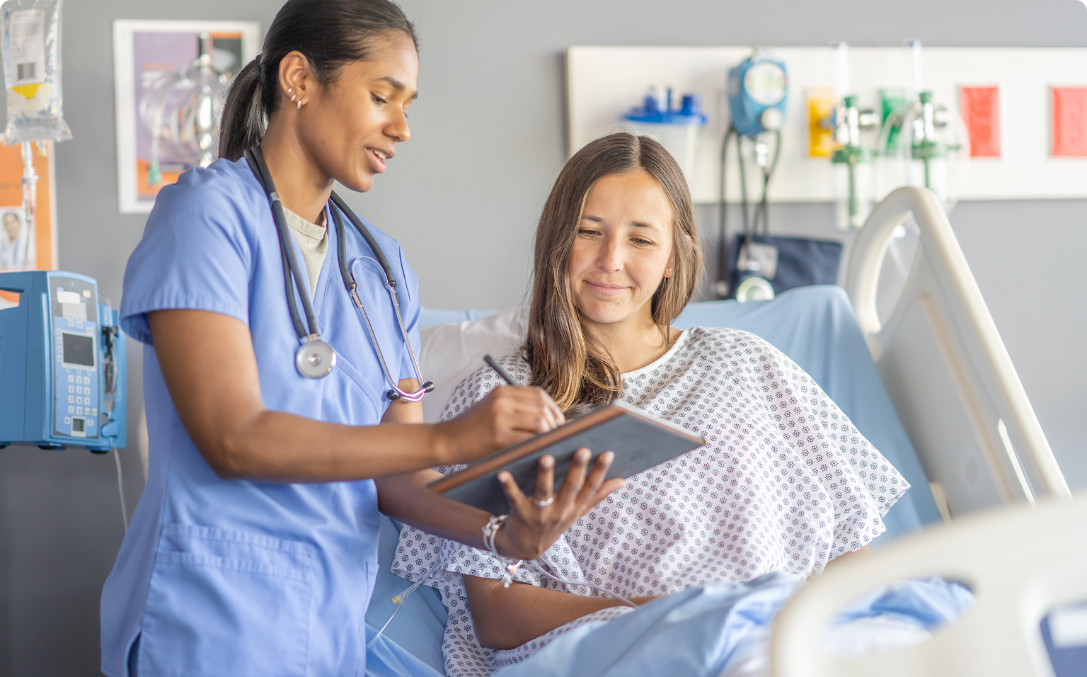 Nurse consulting with patient in hospital bed.